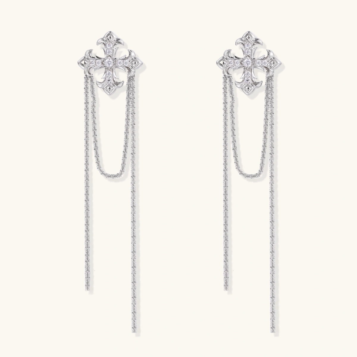 White gold plated baroque cross stud earrings with long cascading zirconia chains on cream background