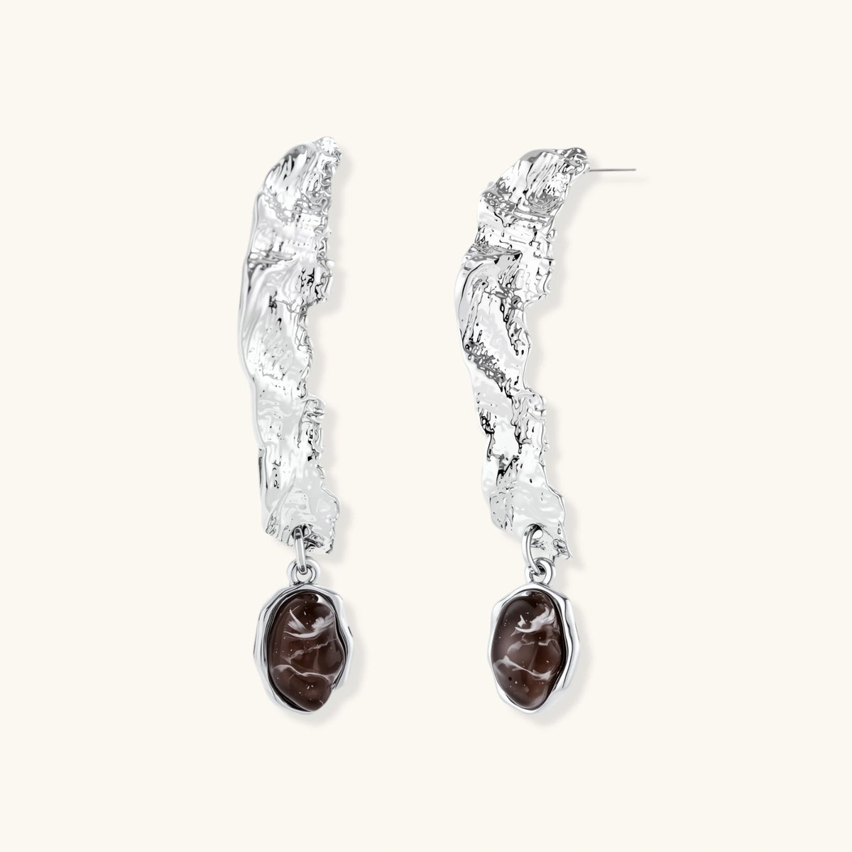 Silver-toned twisted metal earrings with dark brown oval resin stones dangling from sculptural posts on white background.