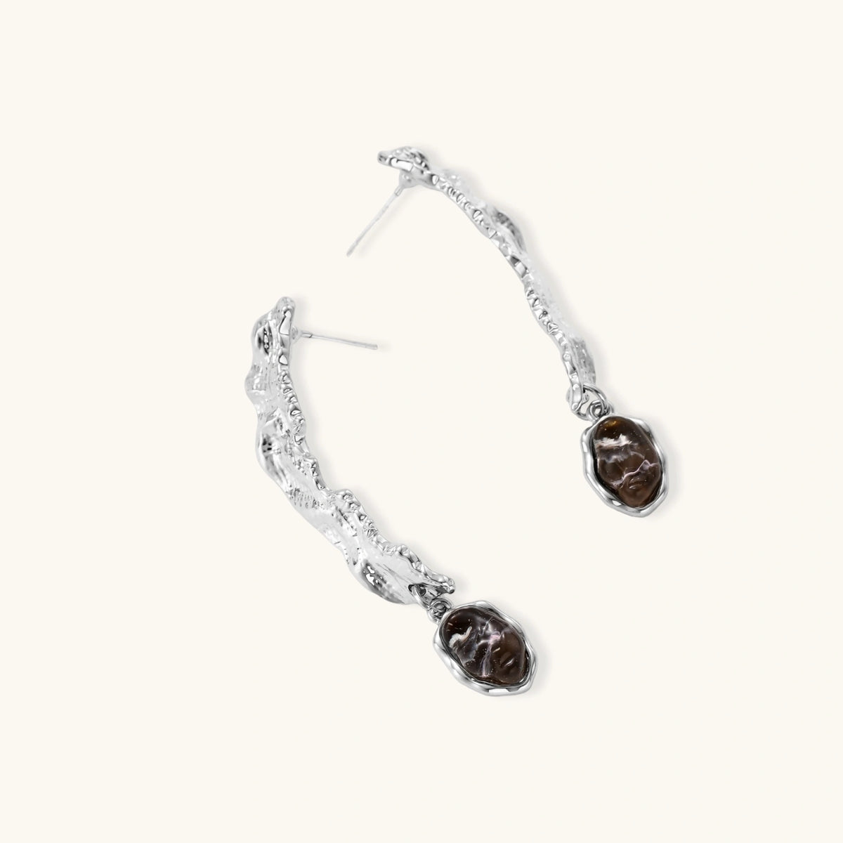 Silver-toned twisted metal earrings with dark brown oval resin stones dangling from sculptural posts on white background.