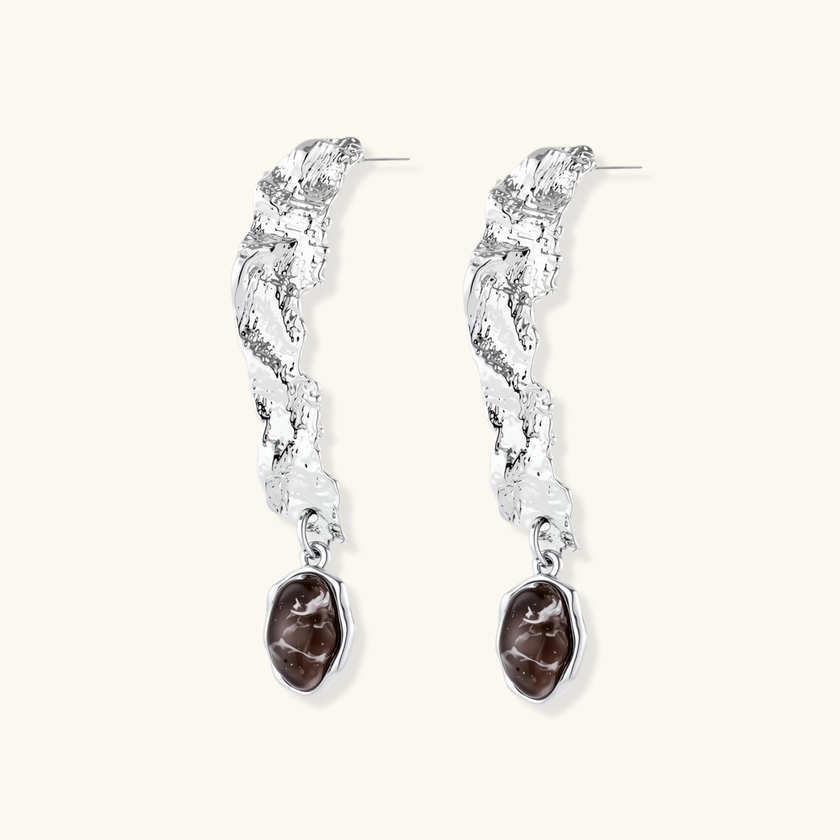 Silver-toned twisted metal earrings with dark brown oval resin stones dangling from sculptural posts on white background.