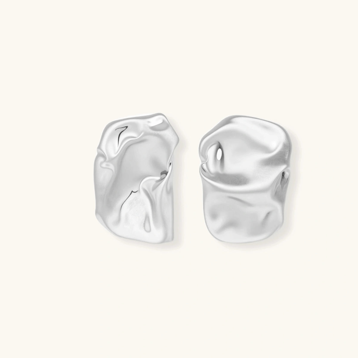 Pair of sculptural silver ear cuffs with organic fluid shapes and polished finish against cream background.