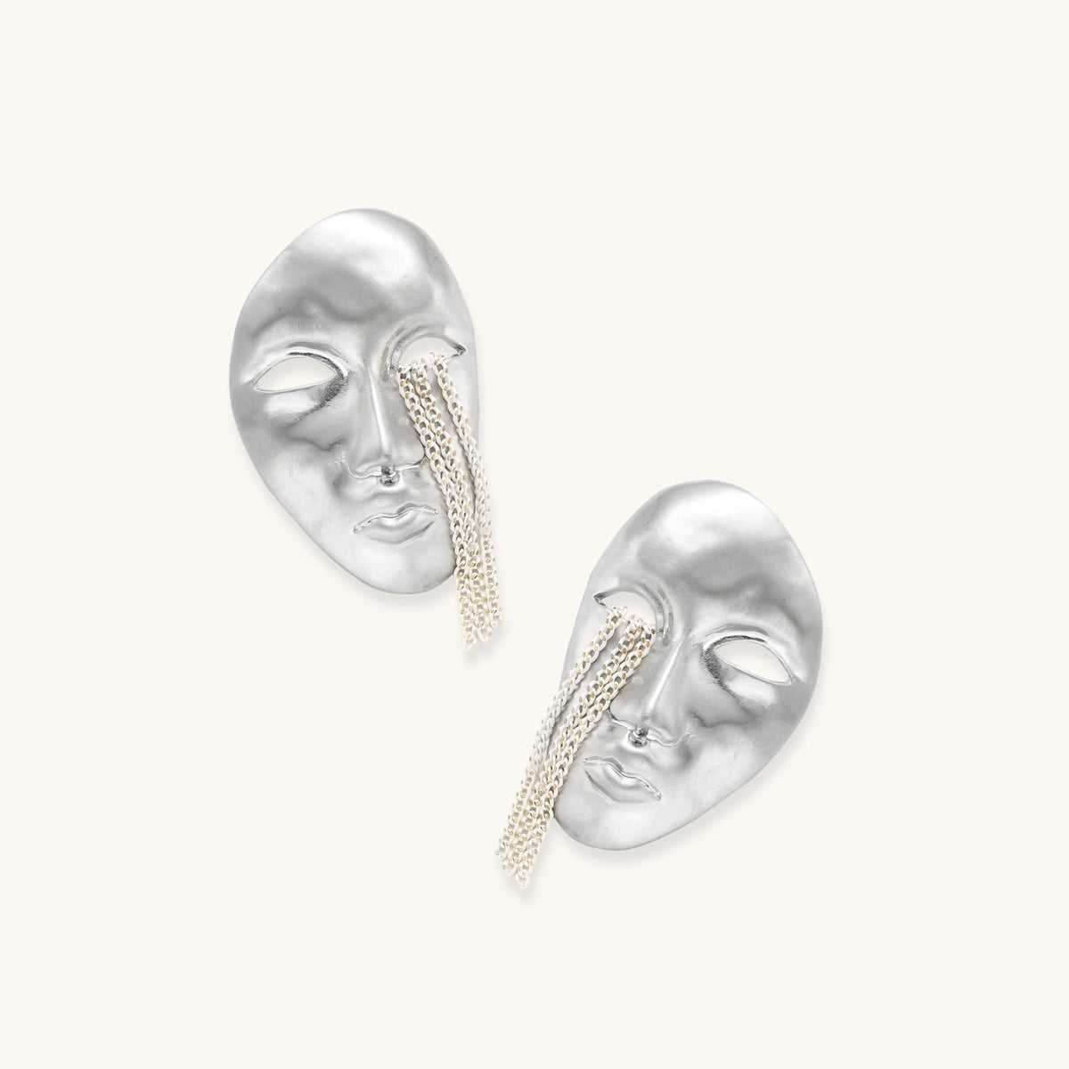 Silver face-shaped statement earrings with flowing chain tassels hanging from sculpted lips on cream background
