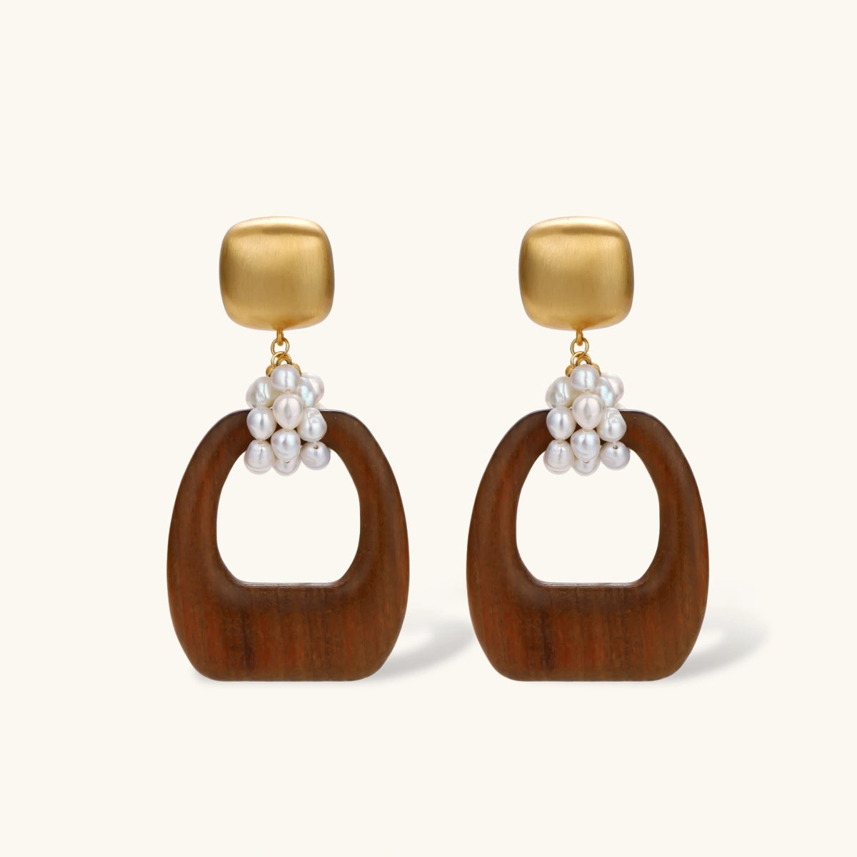 Gold-plated stud earrings with pearl clusters and organic brown wooden hoops on cream background