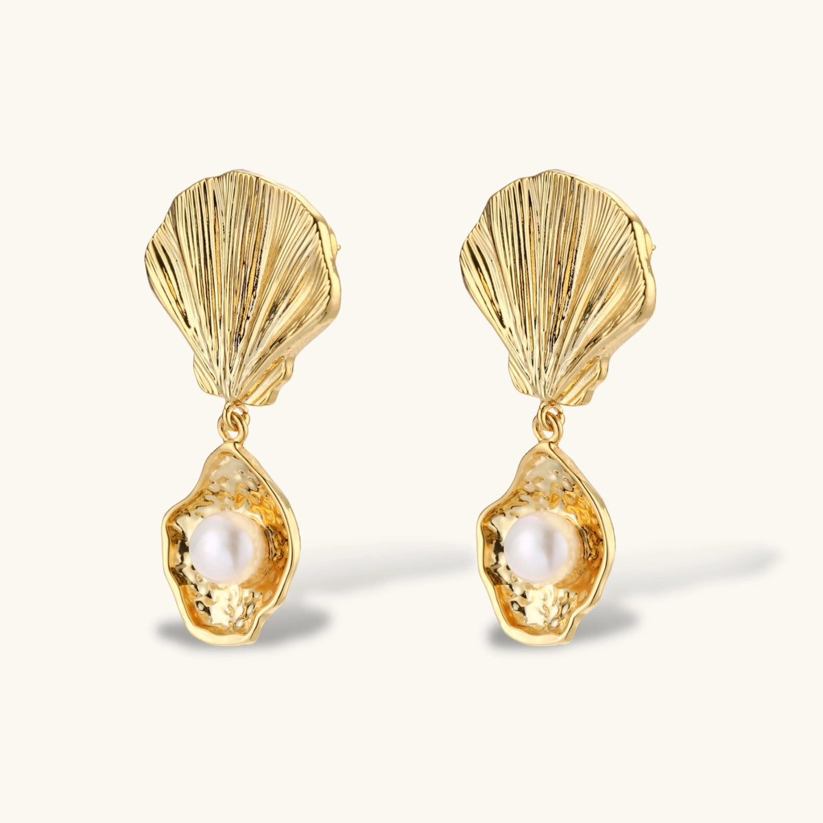 Gold shell-shaped drop earrings with scallop tops and oyster bottoms featuring round freshwater pearls on white background.